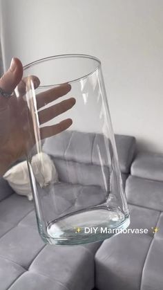 a hand is holding a glass with water in it on top of a gray couch