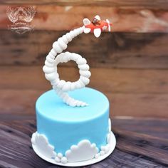 a blue and white cake with an airplane decoration on it's top, sitting on a wooden table