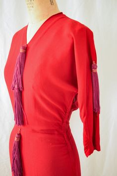 1950s Dress | Arthur Weiss | Vintage Early 50s Dress Red Rayon Wiggle Dress with Purple Tassels  36" Bust DETAILS: *Early 1950s era *Red rayon *Fitted wiggle dress *Dolman sleeve bodice *Waist seam *V-neck *Slight ruching on side seams *Purple (soft not bright or royal) tassels decorate the center front and sleeves *Elbow length sleeves *Unlined *Back and Side metal zipper LABEL: Arthur Weiss CONDITION: A few small holes that have been repaired. A tassel is missing from the front. I have left the string in but could easily be taken out and no one would know that a tassel is missing. Overall great condition for its age.   MEASUREMENTS: Bust= 36" Waist= 28" Hips= 38" Length from high point shoulder to hem= 43" Length from waist to hem= 26" Sleeve length=15" Compare with your own measurements Elegant Red Dress With Fringe, Elegant Red Fringe Dresses, Red Fitted Dress With Tassels, Fitted Red Dress With Fringe, Fitted Red Fringe Dress, Vintage Fitted Dress With Fringe, Fitted Red Dress With Tassels, Fitted Vintage Dresses With Fringe, Purple Soft