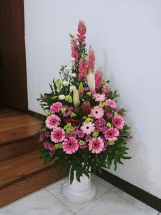 a white vase filled with pink and white flowers on top of a tiled floor next to a wooden door