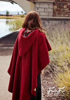 a woman in a red cape is standing by the water