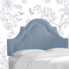 a bed with a blue headboard in front of a floral wallpapered wall