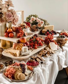 an assortment of cheeses, fruits and crackers on a table with flowers in the background