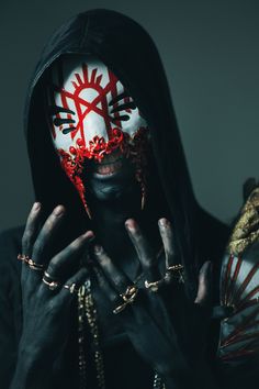 a man in black and white makeup with red accents on his face, holding hands to his face