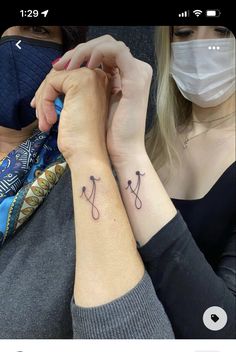 two women wearing masks and holding hands with tattoos on their wrists, one has a stethoscope