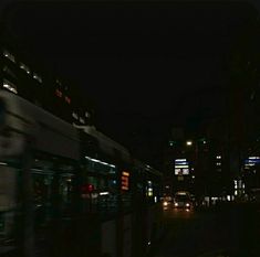 a city street at night with cars and buses passing by in the dark, blurry image