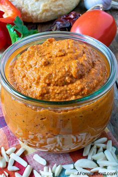 a glass jar filled with sauce sitting on top of a table next to bread and vegetables