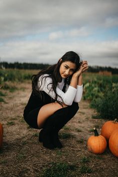 a woman kneeling down next to pumpkins on the ground with her hands in her face