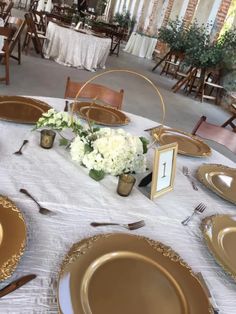 the table is set with gold and white plates, silverware, and flower centerpieces