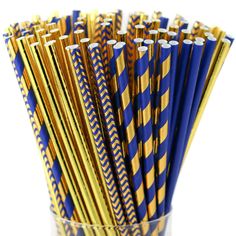 blue and gold striped paper straws in a clear glass vase on a white background