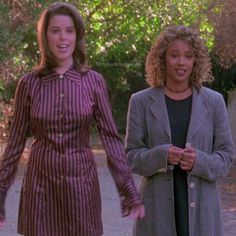 two women standing next to each other on a road with trees in the back ground