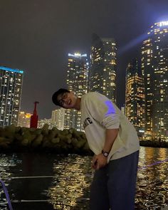 a man standing on the edge of a body of water in front of tall buildings