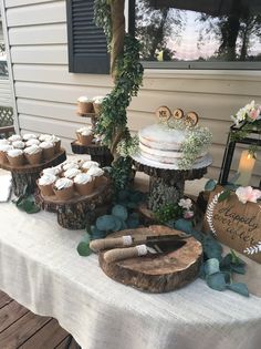 a table topped with cakes and cupcakes on top of wooden slices covered in greenery