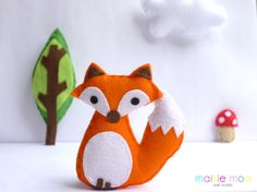 an orange stuffed animal sitting next to a tree and mushroom on a white surface with clouds in the background