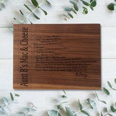 a wooden cutting board with writing on it next to some green leaves and greenery