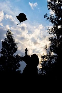 the silhouette of a person flying a kite in the sky with trees and clouds behind them