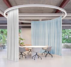 a round table with four chairs in front of a curtained wall and two planters on the other side