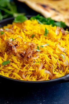 yellow rice with onions and herbs in a black bowl on a blue countertop next to bread