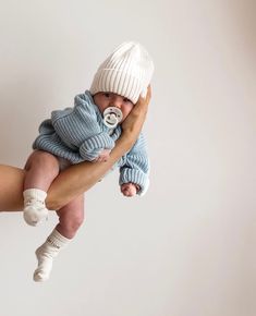 a woman holding a baby wearing a blue sweater and white hat with a pacifier in it's mouth