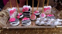 a tray with cake pops decorated like zebra stripes and pink roses on them, sitting on a gold sequin tablecloth