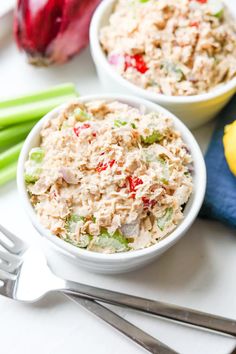 two white bowls filled with tuna salad next to green onions and celery sticks