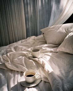 a cup of coffee sits on a bed with white sheets and drapes over it