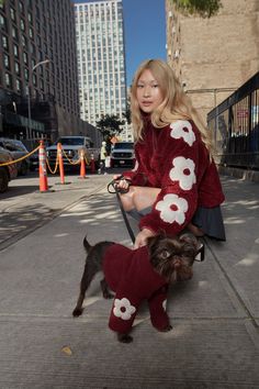 a woman sitting on top of a bench next to a small dog wearing a sweater