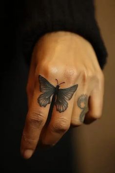 a hand with a small butterfly tattoo on it's left thumb and the middle finger