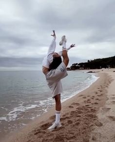 a woman doing a handstand on the beach with her feet in the air