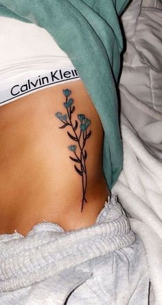 a woman's stomach with a tattoo on her side and flowers growing out of it