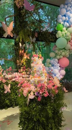 a cake surrounded by balloons and flowers in front of a window with butterflies on it