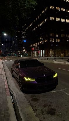 a car is parked on the side of the road at night in front of some tall buildings