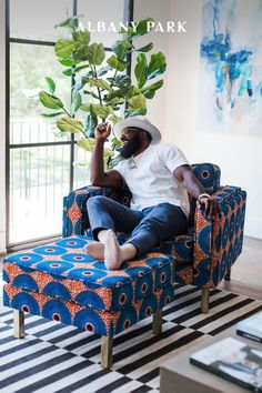 a man sitting on a blue couch in front of a window with a plant growing out of it