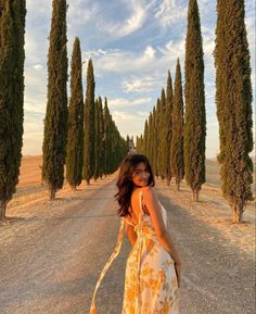 a woman standing in the middle of an empty road with trees lining both sides and behind her