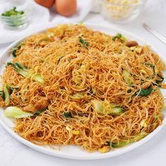 a white plate topped with noodles and veggies next to eggs on a table