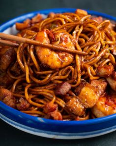 a blue bowl filled with chicken and noodles next to chopsticks on a table