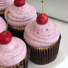 several cupcakes with pink frosting and cherries on top are sitting on a plate