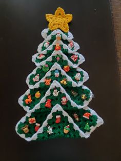 a crocheted christmas tree is displayed on a black surface with white and yellow trim