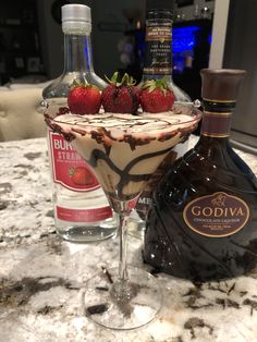 a chocolate martini with strawberries on the rim next to a bottle of booze