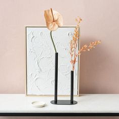 two black vases with flowers in them on a table next to a white plate