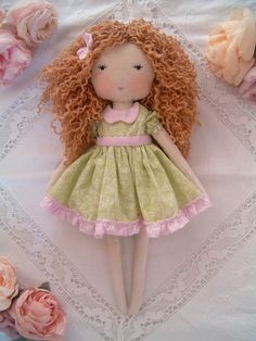 a doll with curly hair laying on a table next to pink flowers and lace doily