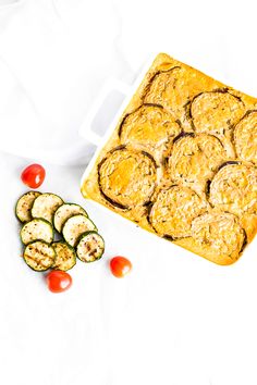 a casserole dish with zucchini and tomatoes on the side next to it