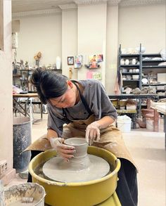 a woman working on a pottery wheel in a room filled with shelves and other items