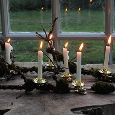 a group of lit candles sitting on top of a wooden table next to a window