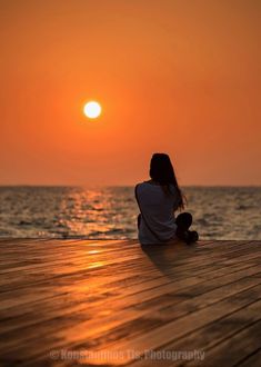 a person sitting on a dock watching the sun set