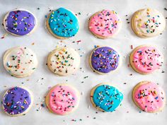 twelve decorated cookies on a baking sheet with sprinkles and colored frosting