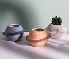 three ceramic pots with plants in them on a white counter top, one has a face drawn on it