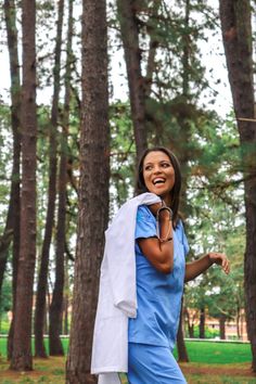 a woman is walking through the woods with a towel on her shoulder and smiling at the camera