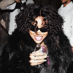 a woman in a black fur coat holding a wine glass and smiling at the camera