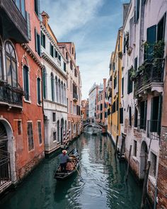 a man in a small boat on a narrow canal between buildings and balconies